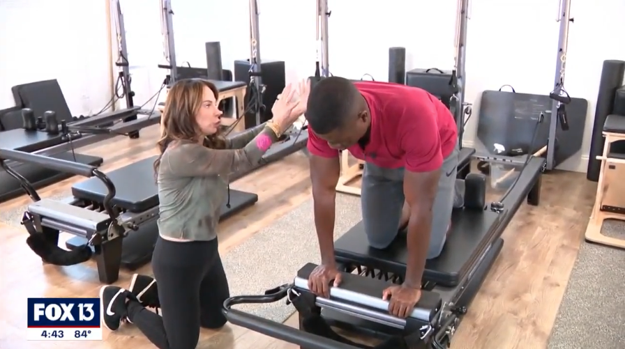 Fox 13 Tampa Bay Tony Sadiku tries out a Pilates Reformer exercise with The Pilates Krewe owner, Sydney Soschin